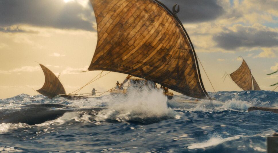 In dieser Szene aus der Vaiana-Realverfilmung segeln mehrere traditionelle Auslegerboote mit großen, braunen Segeln über eine bewegte, tiefblaue See. Die Gischt spritzt hoch, während ein Wal knapp unter der Wasseroberfläche vorbeischwimmt.