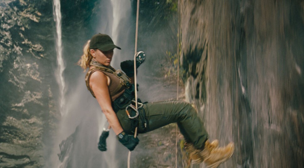 Auf dem Bild siehst Du eine Szene aus Jurassic World: Die Wiedergeburt. Scarlett Johansson seilt sich in Outdoor-Kleidung und mit Sicherheitsausrüstung an einer steilen Felswand ab.
