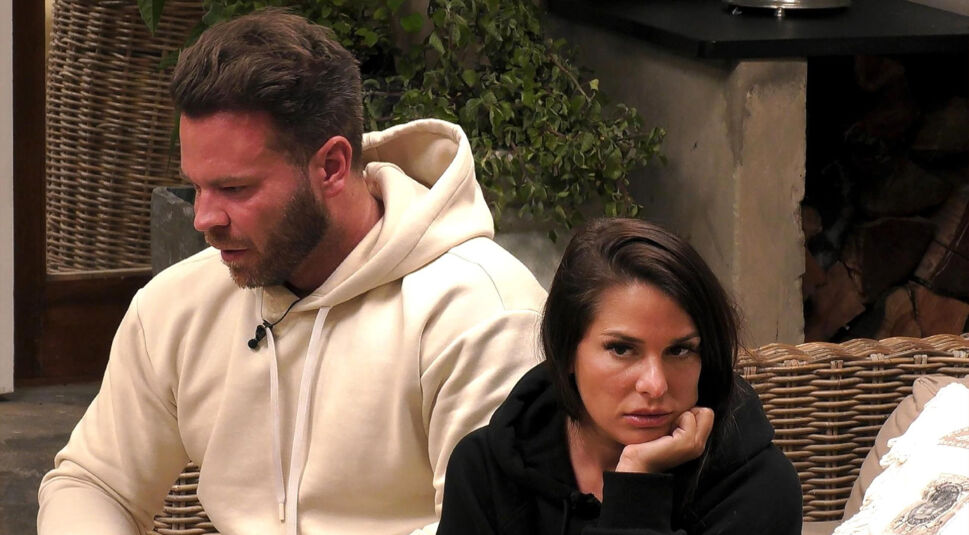 In einem emotionalen Moment aus Staffel 1 von „Prominent getrennt“ (2022) sitzen Meike Emonts und Marcus Muth nebeneinander auf einem Sofa. Marcus schaut ernst nach unten, während Meike mit dem Kopf auf ihrer Hand gestützt direkt in die Kamera blickt. Diese Szene zeigt die Spannungen auf dem Weg der „Prominent getrennt-Gewinner:innen“.