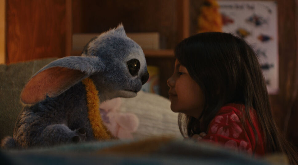 Auf dem Bild in dem Artikel zum Lilo & Stitch-Vergleich ist eine emotionale Szene aus der Live-Action-Version von 2025 zu sehen. Stitch und Lilo blicken sich innig in die Augen, ihre Nasen fast aneinandergestoßen. Lilo trägt ein rotes Hawaii-Kleid, während Stitch einen flauschigen gelben Schal um den Hals hat.