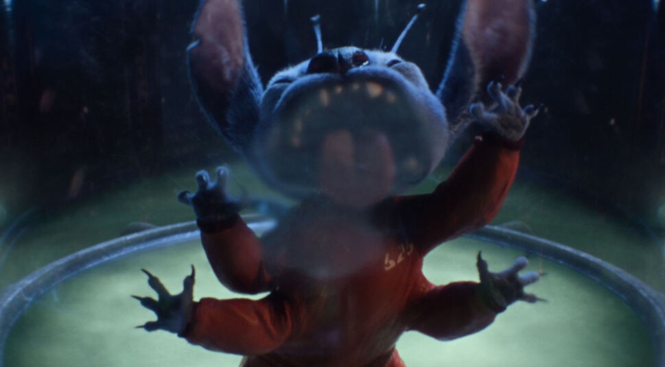 Auf dem Bild in dem Artikel zum Lilo & Stitch-Vergleich ist Stitch in der Live-Action-Adaption von 2025 zu sehen. Die Figur trägt einen roten Raumanzug und ist in einer Glaskammer eingesperrt. Mit gefletschten Zähnen und ausgebreiteten Armen wirkt Stitch wild und bedrohlich.