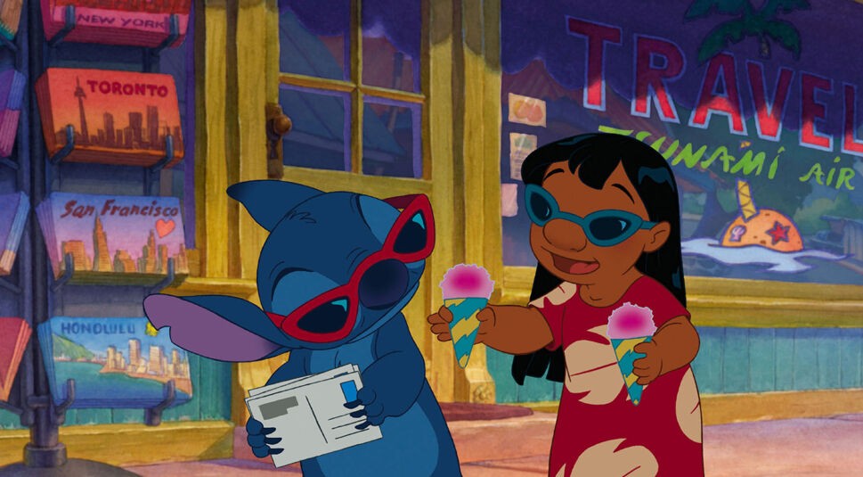 Auf dem Bild in dem Artikel zum Lilo & Stitch-Vergleich sind Lilo und Stitch in der Originalversion von 2002 in einen sommerlichen Moment vor einem Reisebüro zu sehen. Beide tragen Sonnenbrillen – Stitch liest eine Postkarte, Lilo hält Eis in der Hand und lacht.