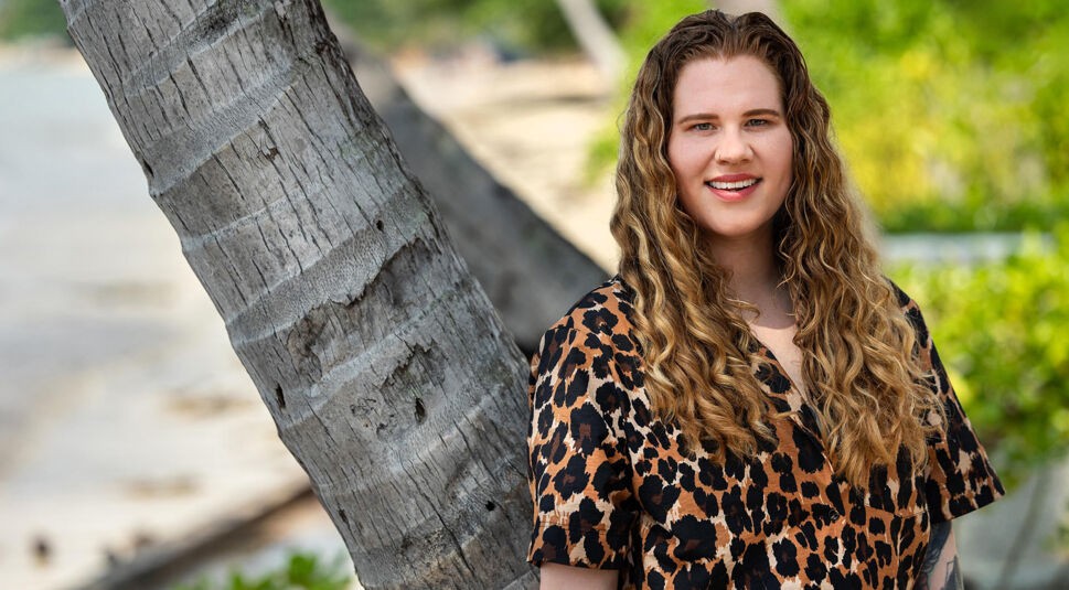 Auf dem Bild in dem Artikel zu Princess Charming 2025 lehnt eine Person mit Leopardenhemd an einer Palme.