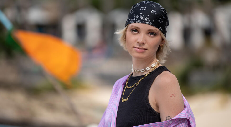 Auf dem Bild in dem Artikel zu Princess Charming 2025 steht eine Person mit lila Hemd am Strand.