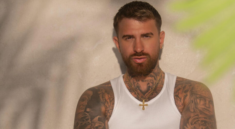 Auf dem Bild zur Villa der Versuchung ist Gigi Birofio vor einer beigen Wand zu sehen. Er trägt ein weißes Shirt und eine goldene Kette.