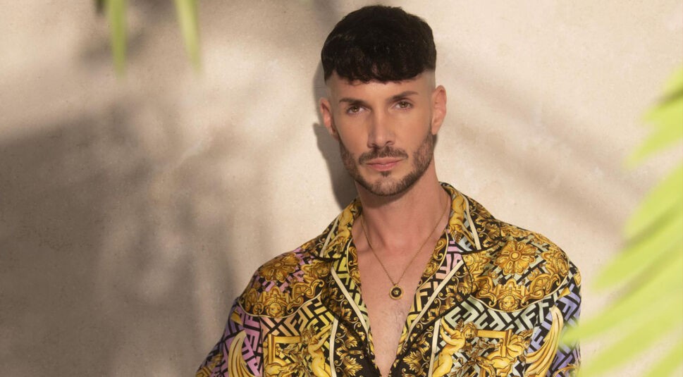 Auf dem Bild zur Villa der Versuchung ist Kevin Schäfer vor einer beigen Wand zu sehen. Er trägt ein auffälliges, bunt gemustertes Hemd sowie eine goldene Kette mit rundem Anhänger. Er schaut ernst in die Kamera.