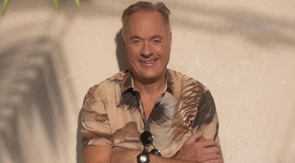 Auf dem Bild zur Villa der Versuchung steht Ronald Schill vor einer beigefarbenen Wand. Er trägt ein kurzärmliges Hemd mit Palmenmuster, Sonnenbrille und Armbanduhr. Er lächelt leicht und hat die Arme locker verschränkt.