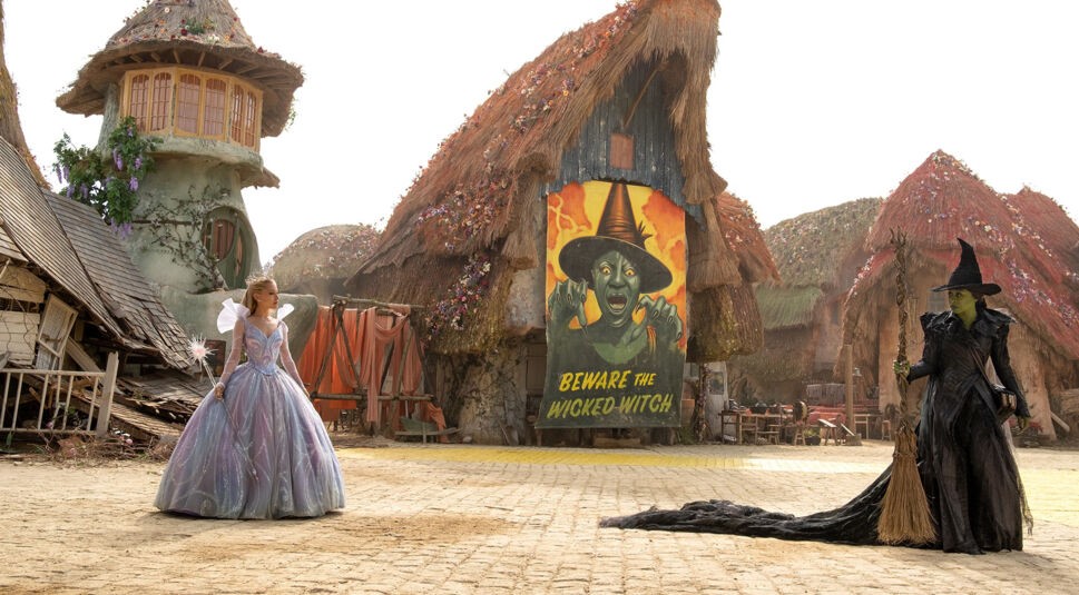 Auf dem Bild in dem Artikel zur „Wicked: Teil 2“-Kritik stehen sich Glinda (Ariana Grande) und Elphaba (Cynthia Erivo) auf einem Dorfplatz gegenüber.