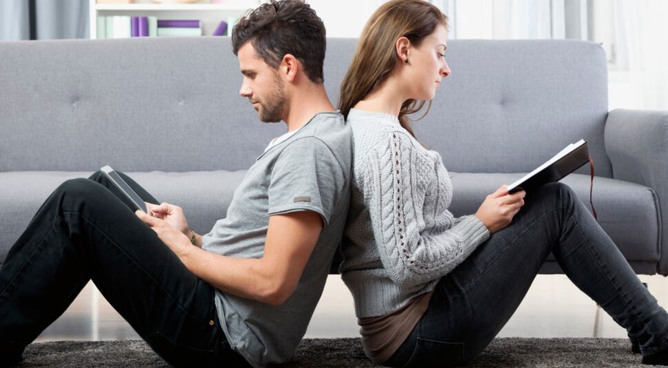 Young couple sitting back to back reading book