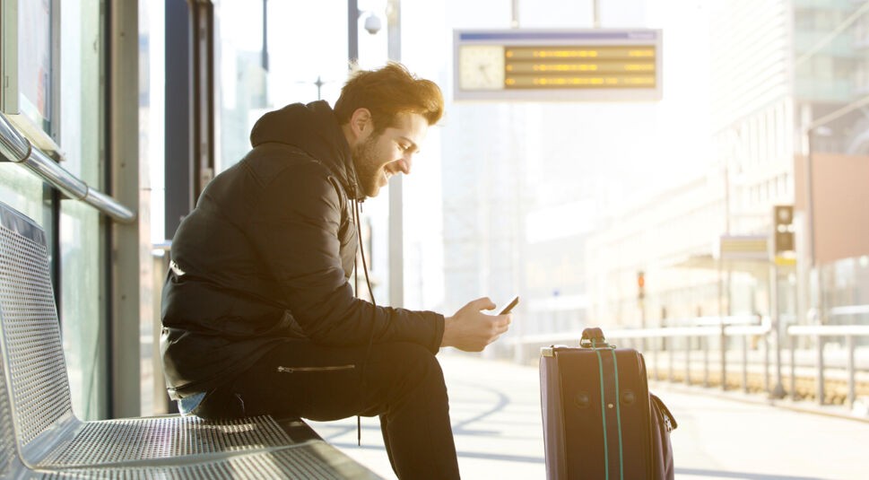 Smiling young man with mobile phone and bag
