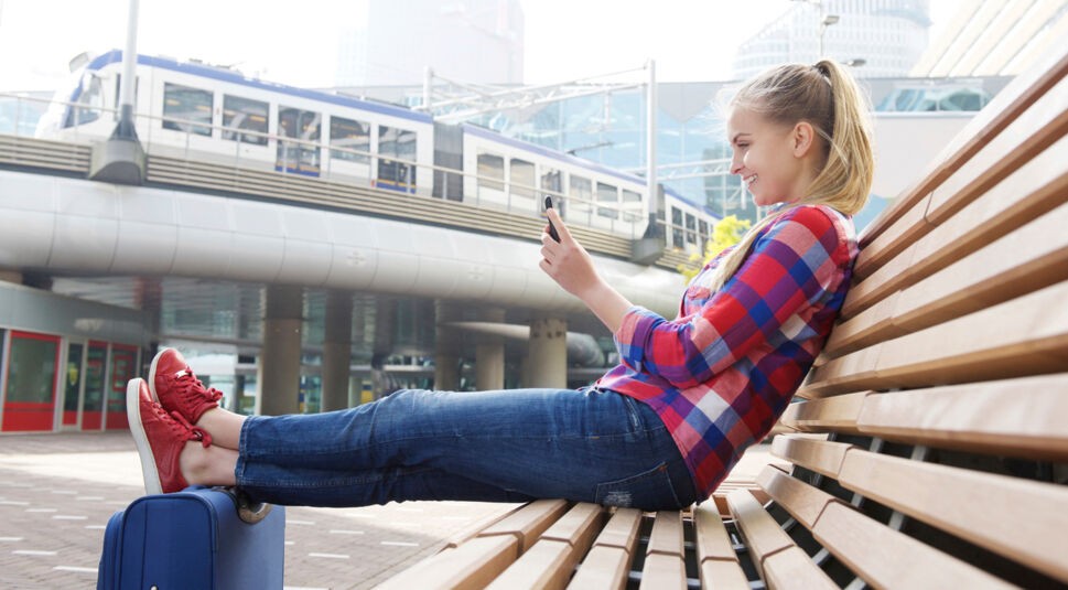 Smiling travel woman sitting outside with mobile phone