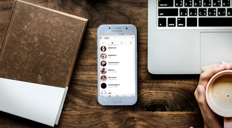 Samsung-Smartphone mit Instagram-Screenshot liegt neben dem Laptop auf dem Schreibtisch.