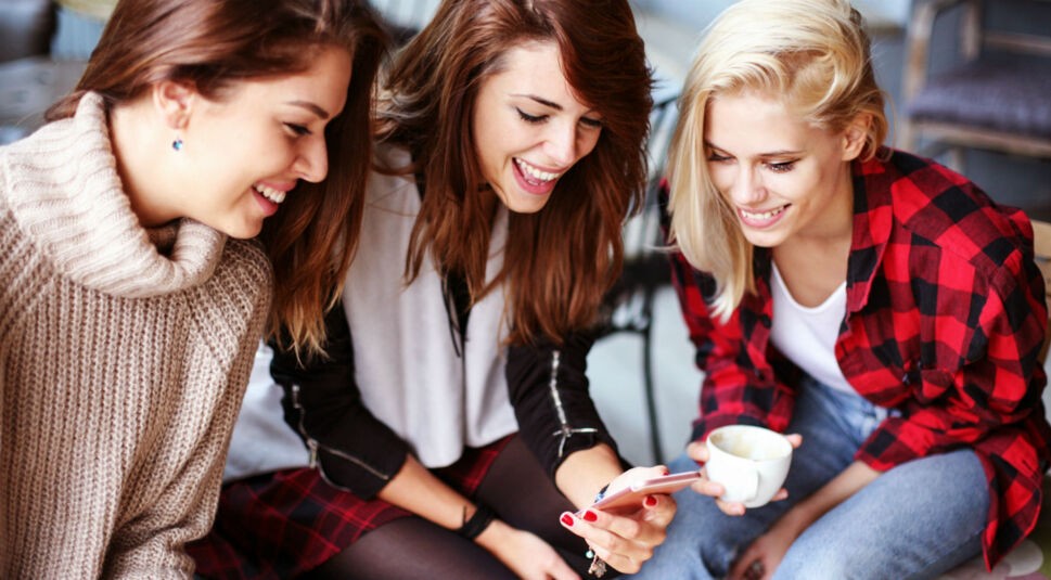 Drei Freundinnen schauen auf ein Smartphone.