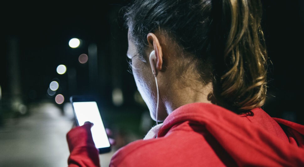 Frau im roten Pulli und Kopfhörern am Smartphone