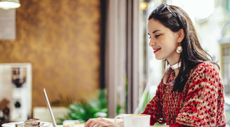 Junge Frau in roter Kleidung und Kaffee sitzt vor dem Laptop.