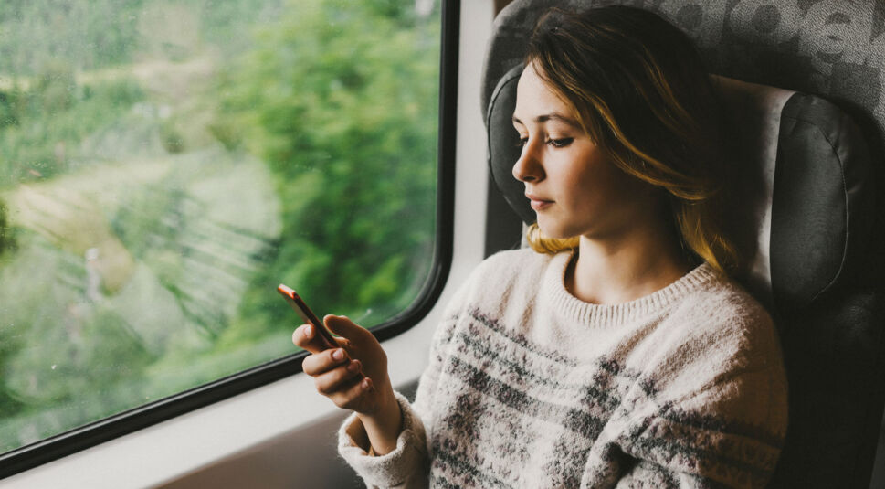 Frau schaut im Zug nachdenklich aufs Smartphone.