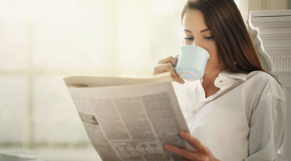 Frau trinkt Kaffee und schaut auf eine Zeitung.