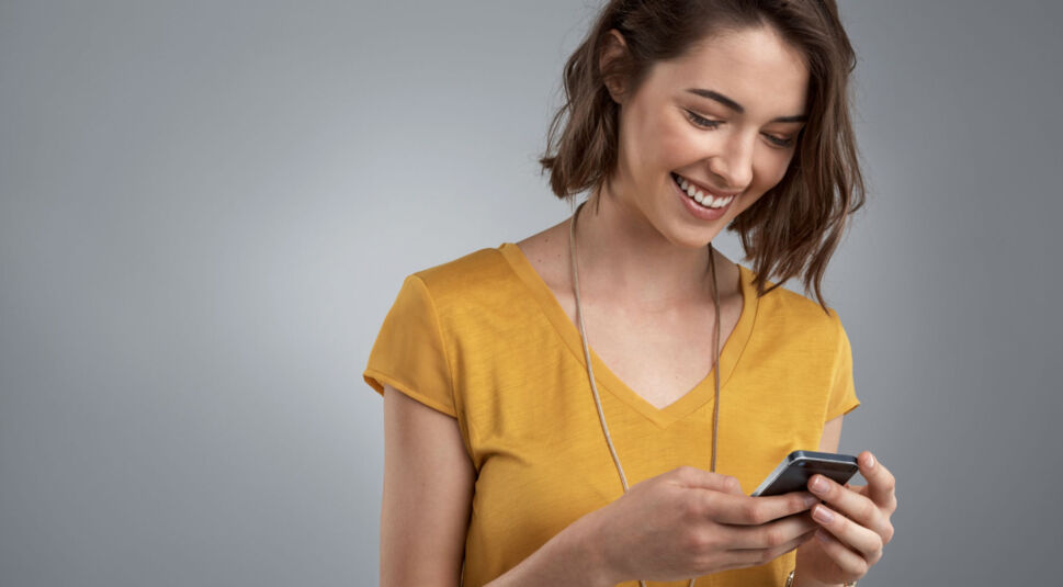 Junge Frau lächelt und schaut aufs Smartphone.