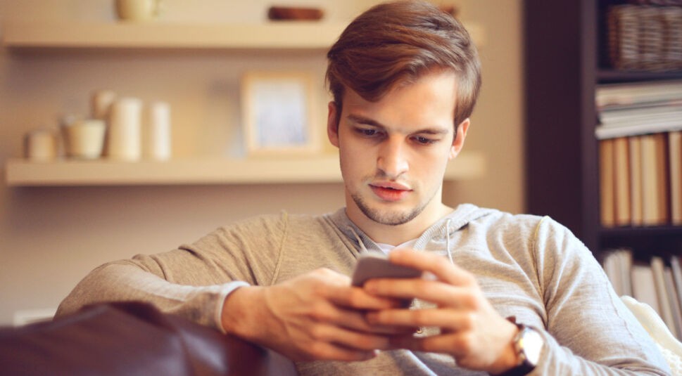 Junger Mann spielt mit Smartphone auf dem Sofa.