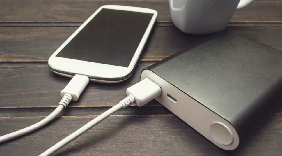 Powerbank lädt Smartphone, daneben steht eine weiße Tasse.