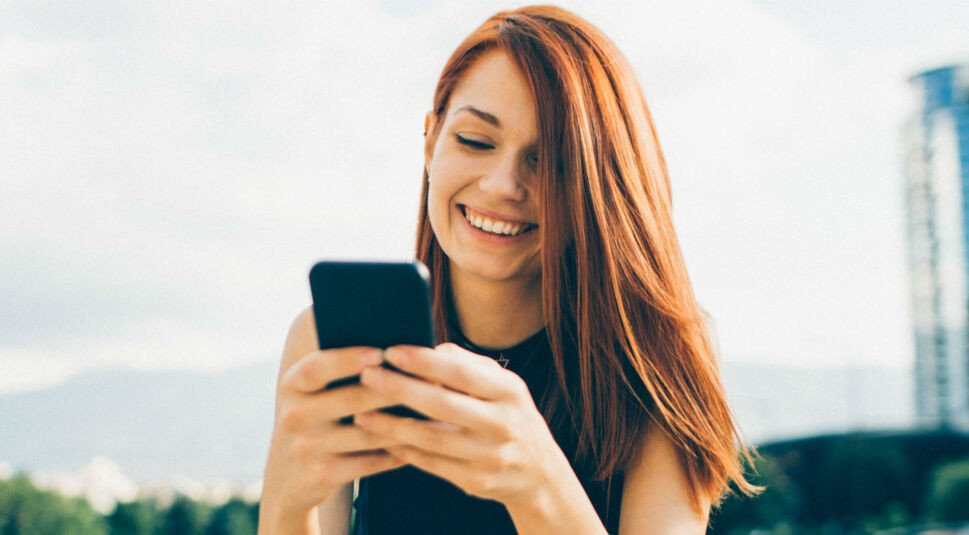 Rothaarige Frau mit Smartphone in der Hand