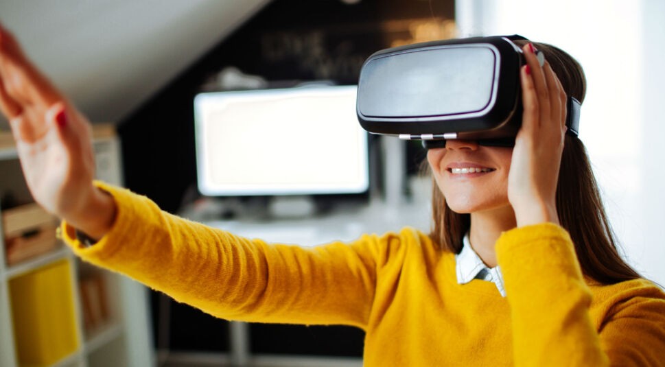 Frau im gelben Pulli trägt VR-Brille.