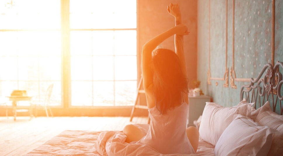 Frau streckt sich im Bett.