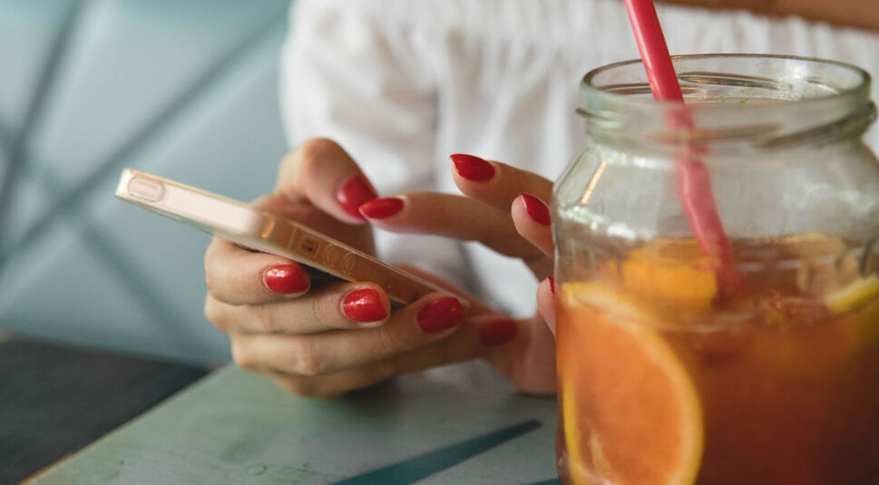 Frau mit lackierten Nägeln hält iPhone in der Hand.