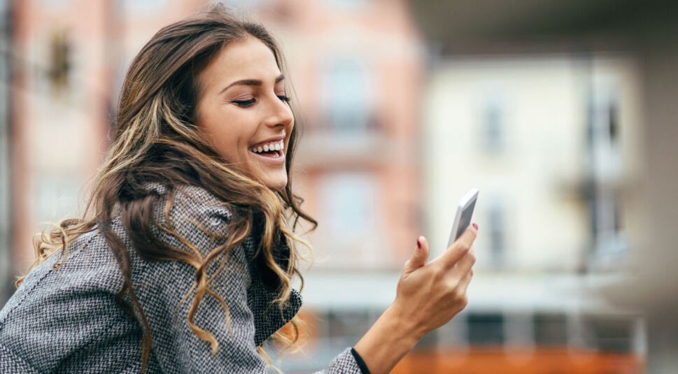 Junge Frau lächelt und schaut auf ihr Smartphone.