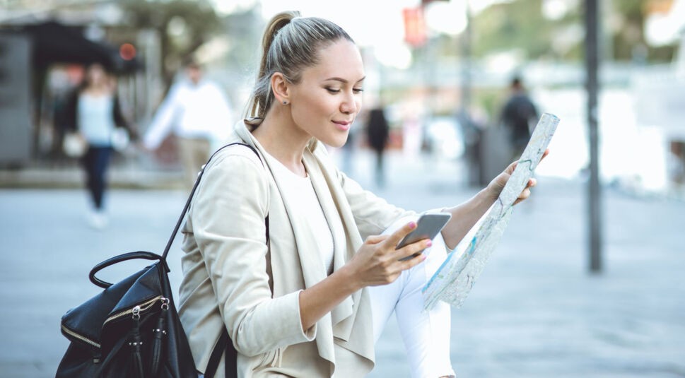 Junge Frau orientiert sich mithilfe von Stadtkarte und Smartphone.