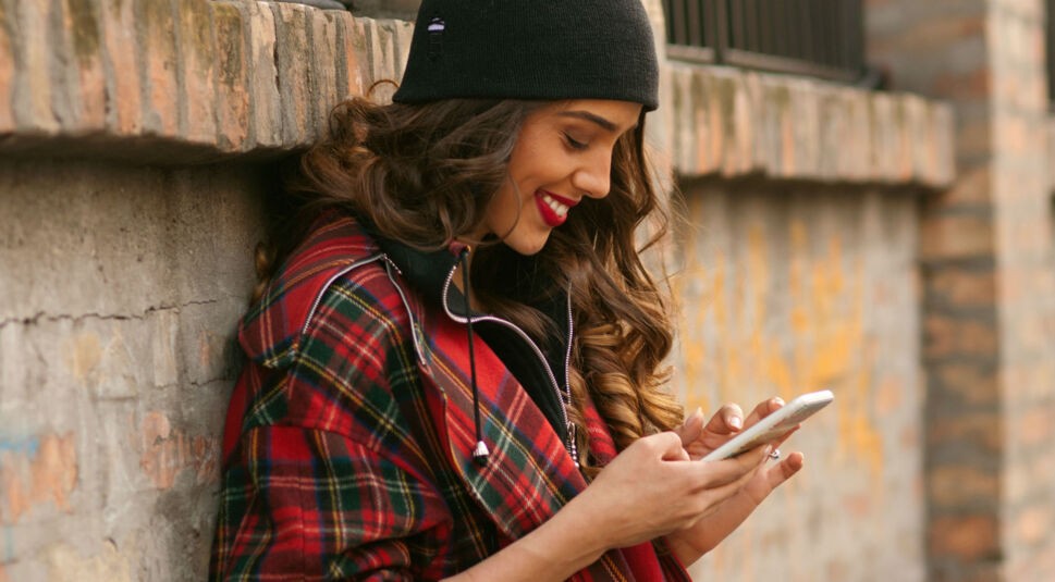 Junge Frau in kariertem Hemd schaut auf Smartphone.