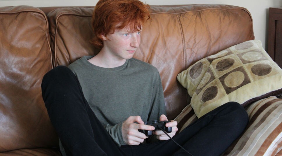 Junge mit roten Haaren zockt per Controller in der Hand.