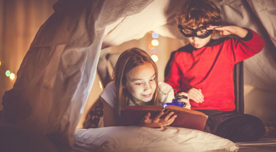 Zwei Kinder mit einer Taschenlampe lesen ein Buch.