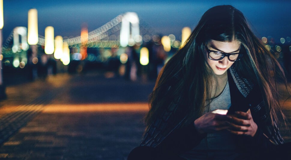 Junges Mädchen schaut auf ihr Smartphone in der Nacht.