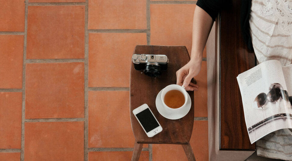 iPhone, Tasse Tee und Kamera liegen auf Hocker aus Holz.