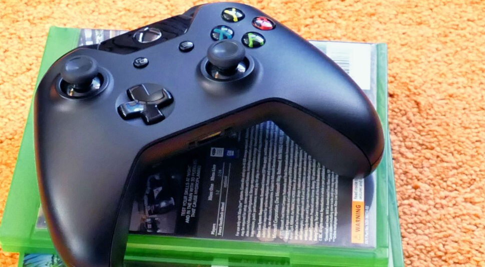 Xbox One Controller auf einem Haufen Spiele auf gelbem Teppich.