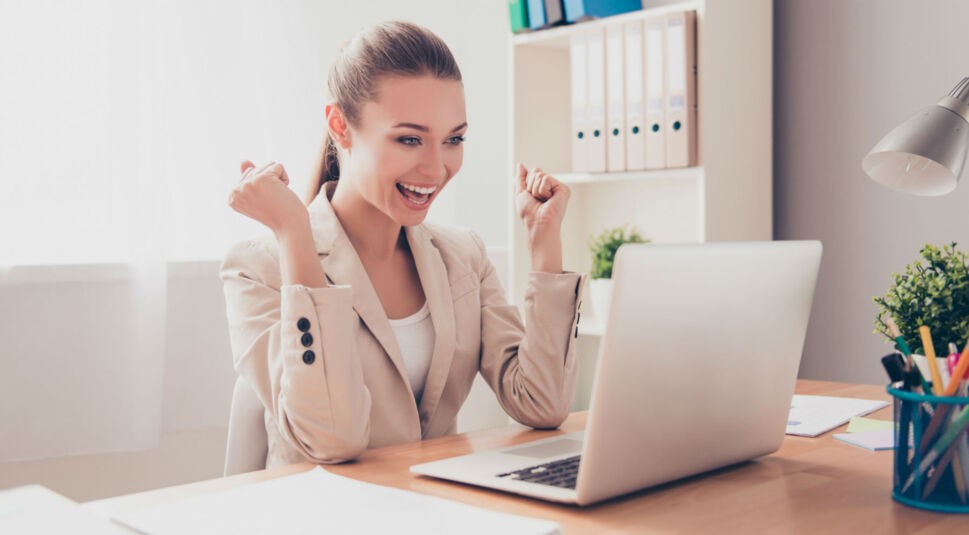 Junge Frau hebt begeistert die Hände, vor ihr steht das Laptop.