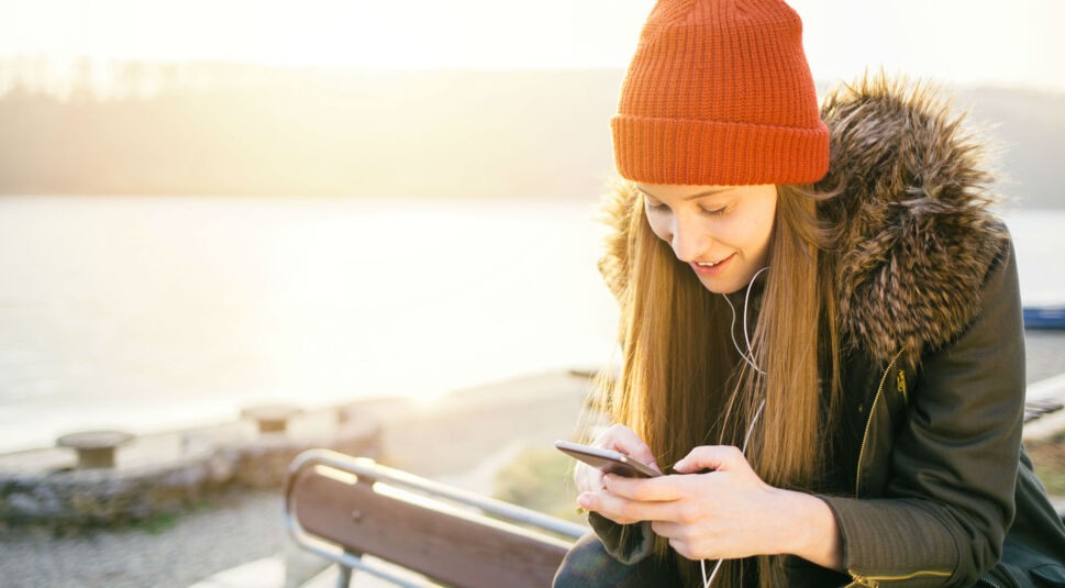 Junge Frau in grünem Parka schaut auf ihr Smartphone.