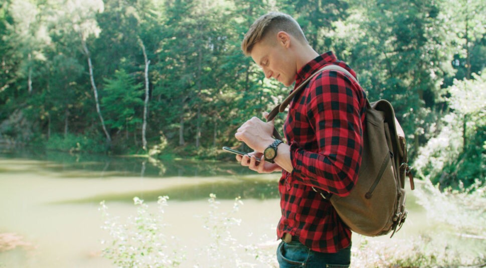 Junger Mann ist draußen unterwegs und schaut auf sein Smartphone.