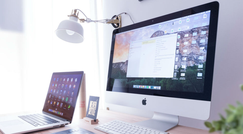 Ein Mac-Computer steht auf einem Schreibtisch, daneben eine Lampe.