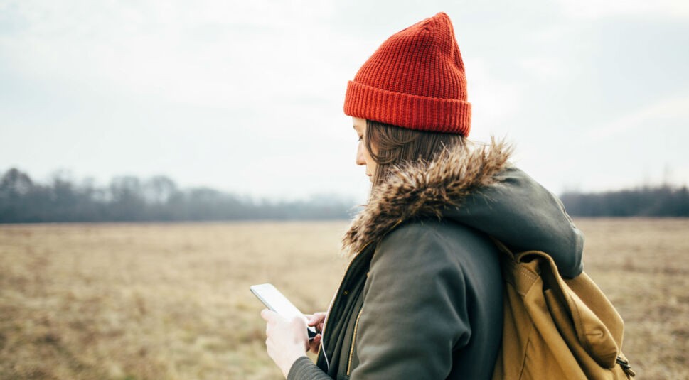 Junge Frau ist draußen unterwegs und schaut auf ihr Smartphone.