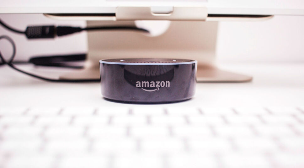 Schwarzer Amazon Echo Dot steht auf dem Schreibtisch vor dem Computer.