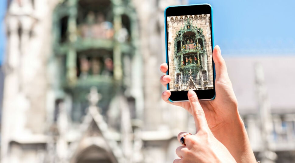 Menschliche Hand schießt ein Foto vom Münchener Rathaus mit dem Smartphone.