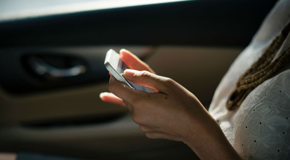 Junge Frau sitzt im Auto und schaut auf ihr iPhone.
