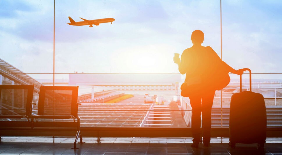 Junge Frau steht mit Kaffeebecher in der Hand am Flughafen.