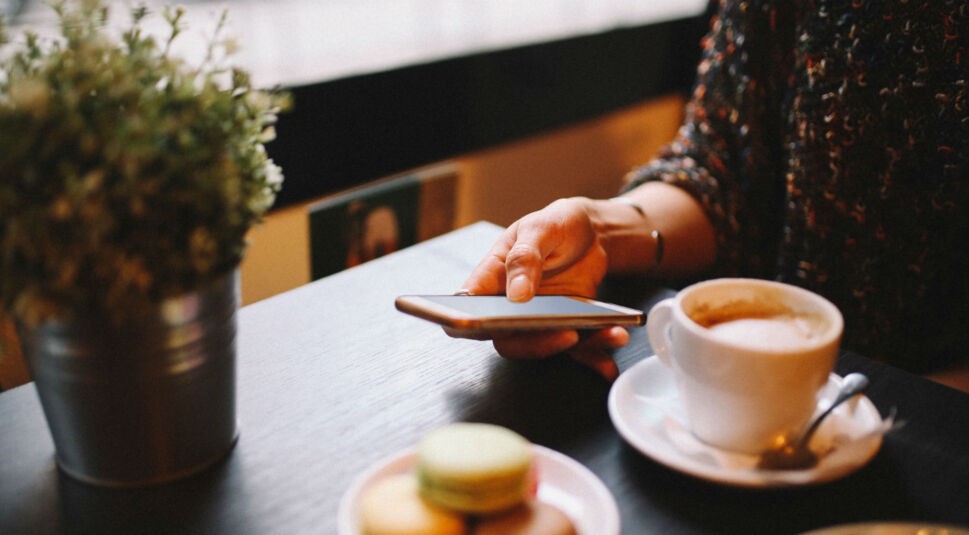 Junge Frau öffnet die Alexa-App auf dem Smartphone am Frühstückstisch.