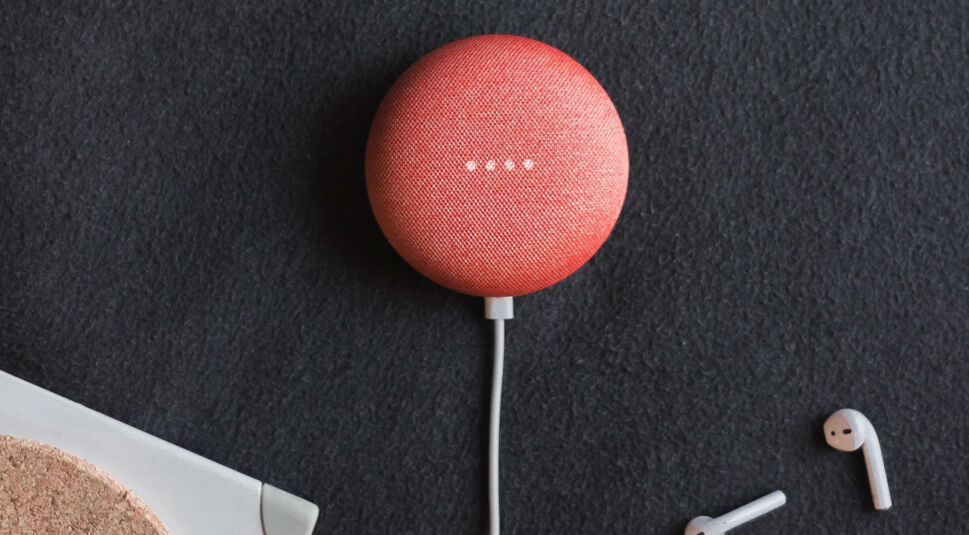 Korallenfarbener Google Home-Mini liegt auf einem schwarzen Schreibtisch.