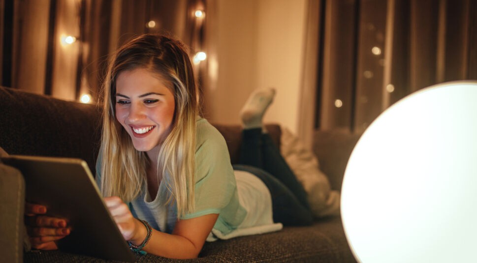Eine Frau liegt entspannt mit einem iPad auf dem Sofa