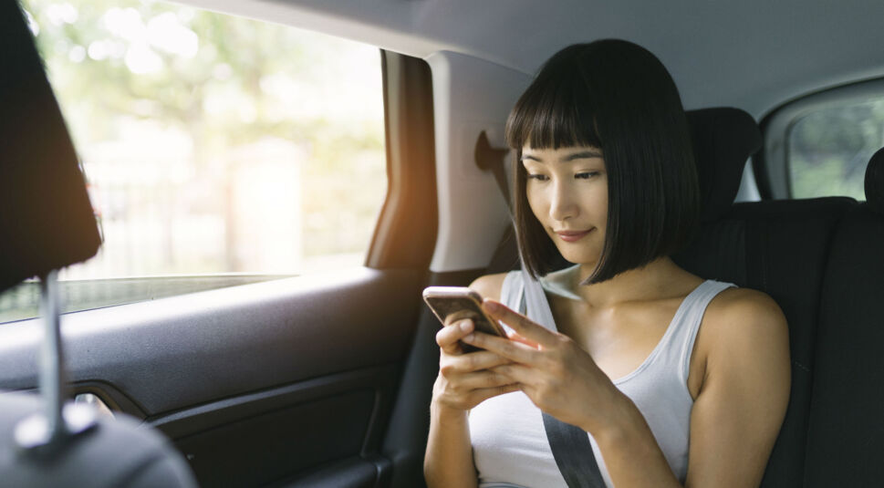 Junge Frau spielt am Smartphone, während sie im Auto sitzt.