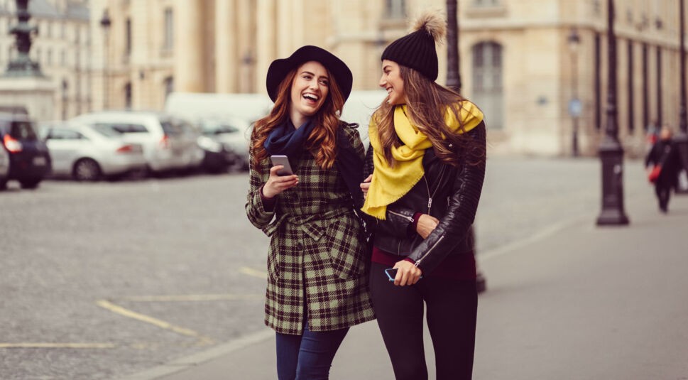 Freunden sind spazieren und lachen über eine WhatsApp-Nachricht auf dem Smartphone.